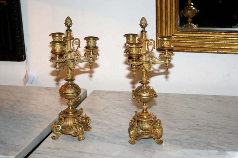 Pair of 19th century Louis-Phillipe ormolu three-light candelabras centered by pineapple finial, finely scalloped bobeches with turned pendant on ovoid shaped stem fitted with ring decoration, outscrolled quadruple footed base.