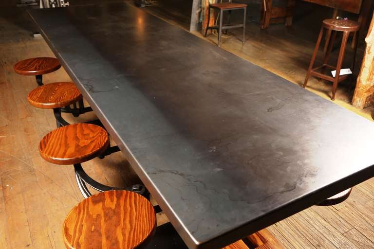 Industrial cast iron and wood swing out suspended seat / stool dining table with steel top. Can bolt to the floor for maximum stability. Douglas fir beams, alder seats (other material available). Please contact us for sizing & material options.