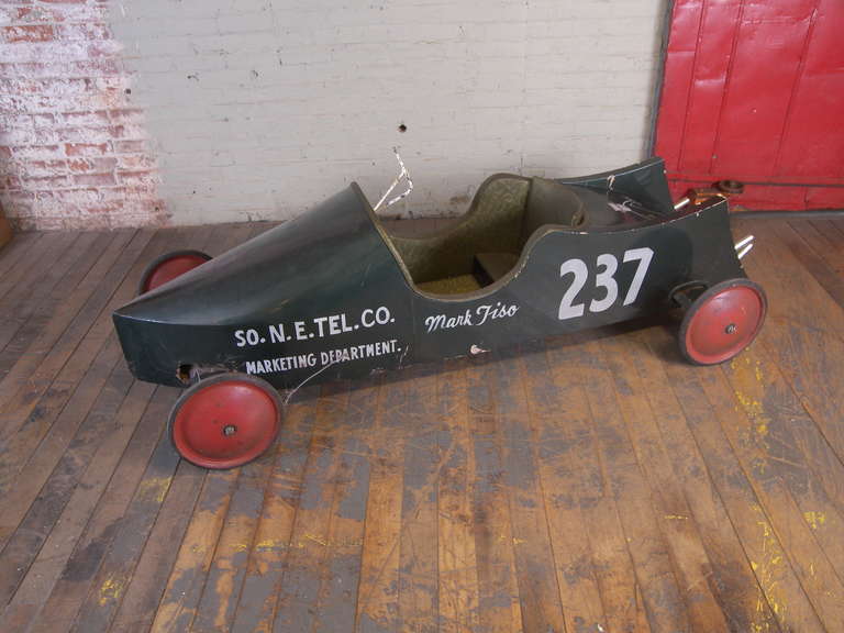 1968 Soap Box Derby Car.  Dark green paint with red wheels.  Needs some attention as the steering wires have been cut and the inside could use a cleaning.  Original program and helmet included.