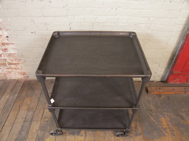 Vintage industrial cast iron rolling serving bar cart, table on cast iron swivel castors, wheels castors. Three tiers or shelves, bottom two are adjustable in height. Top measures: 25 3/4