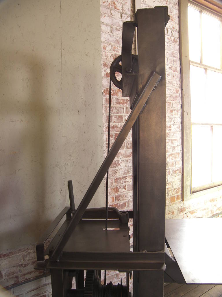 Vintage Industrial steel manual die lift table. Overall dimensions are 51" x 24" x 79". Adjustable shelf measures 27 1/2" x 24". Shelf is adjusted by the hand crank at the back of the table. On castors.