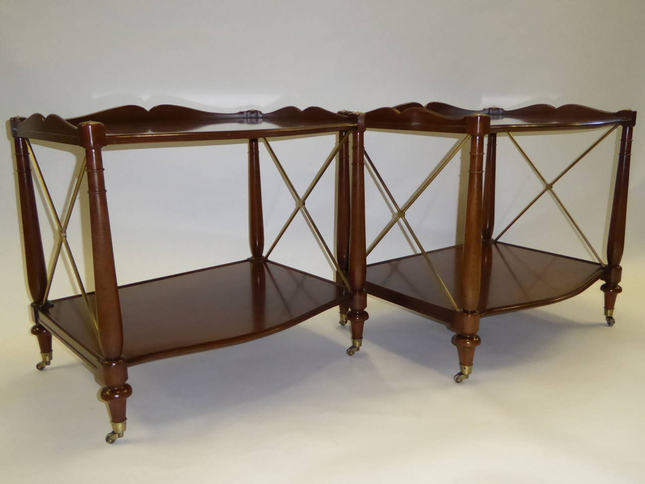 Refined & elegant pair of Regency style tables in lathe turned & molded walnut with solid brass mounts and casters.  With a sculpted gallery around the top, great scale and roomy stretcher shelf below, they make perfect nightstands or bedside tables