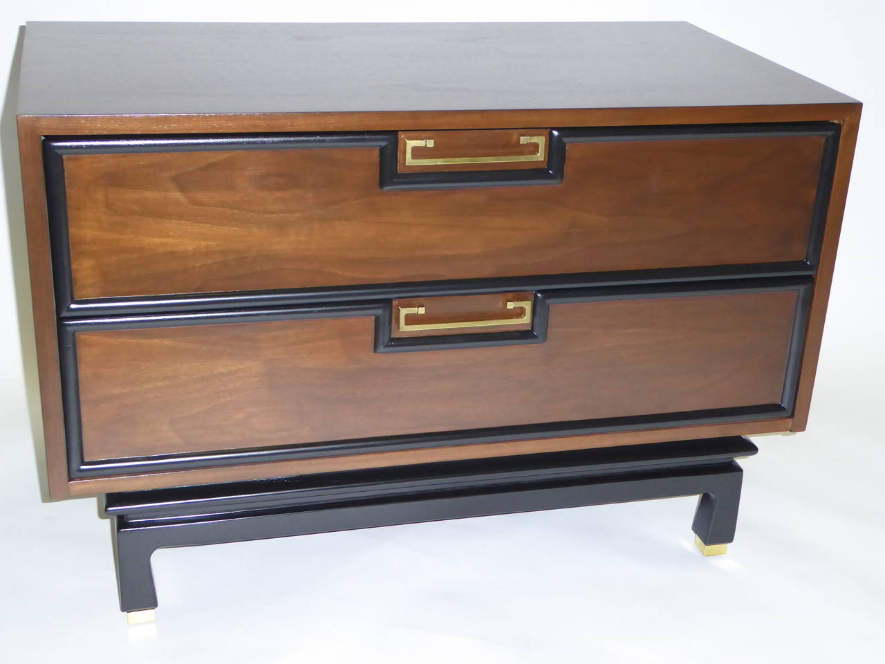 SOLD  Fine PAIR of great scale mid-century modern two drawer bedside tables in walnut with brass pulls and sabots.  These nightstands are accented around the drawers with black molding and a sculpted base with a slight Asian flair.  Beautifully