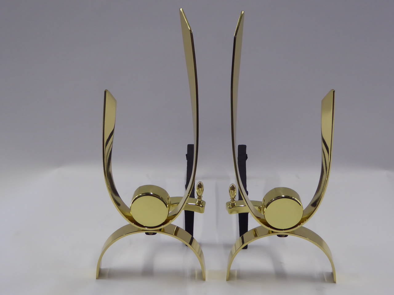 Thick polished brass ribbons arched and curved with a centered disc highlight this pair of andirons attributed to Donald Deskey. Freshly polished brass and re-blacked iron. Each disc with small split in brass (soldered