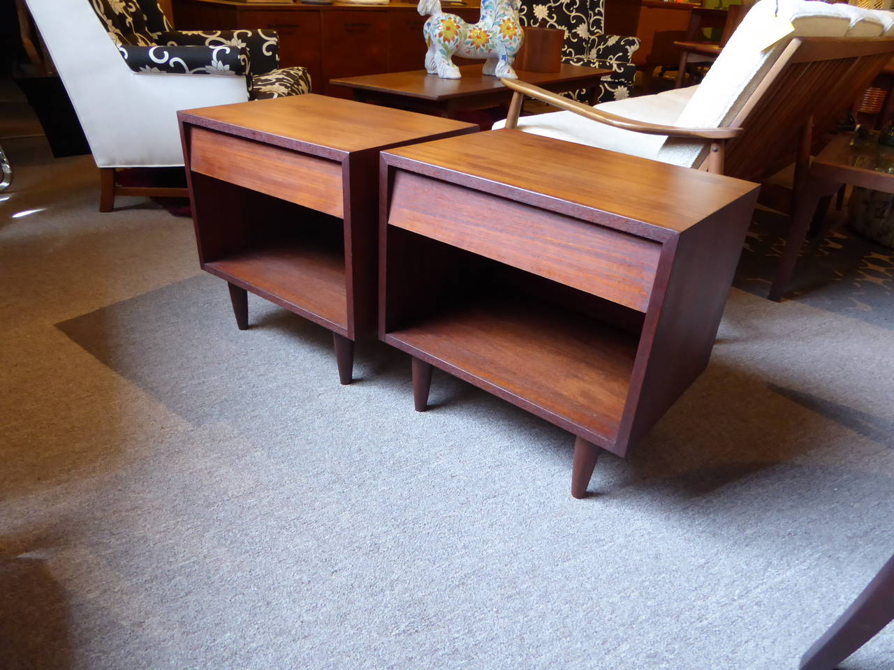 SOLD  Nice Minimalist Danish styling in this pair of warm and figured teak bedside tables, each with a single Knoll style slant front drawer over an open cabinet raised on tapered legs. In excellent condition with two small veneer repairs to the