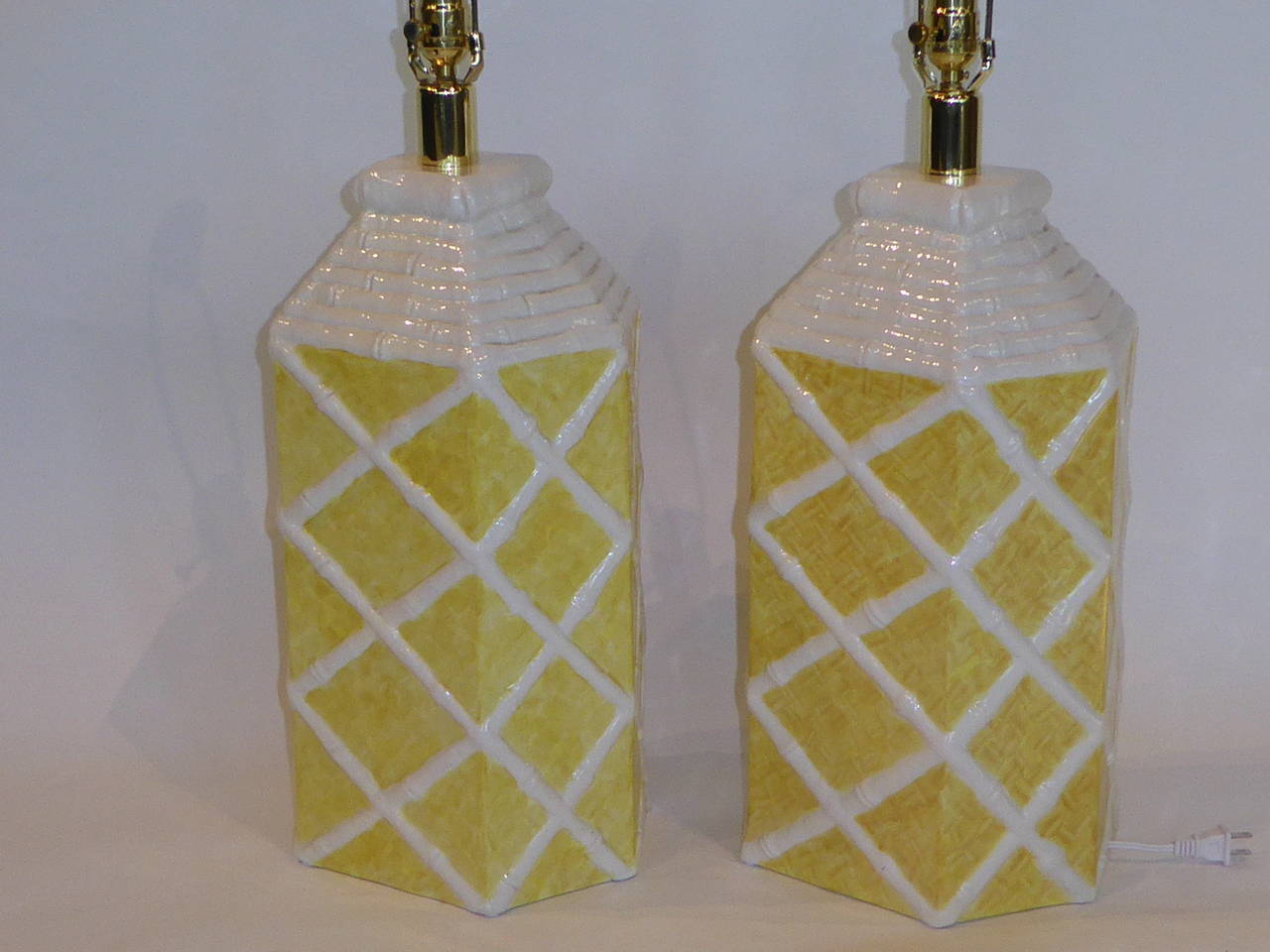 Sunny 1960s Billy Baldwin and Palm Beach style ala a touch of chinoiserie with this pair of signed ceramic table lamps. Elongated hexagonal in shape they have a painted cane background criss-crossed with raised bamboo lattice. Signed Townsends for