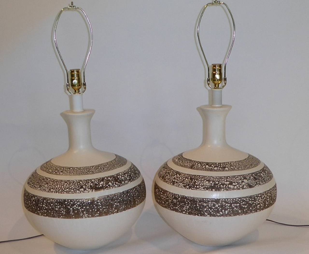 Really fat and fun vase form pottery lamps in a creamy white glaze with three concentric bands of unglazed dark chocolate brown splattered and dripped with the white glaze covering the rest of the body. Great lava glaze piece of the period.