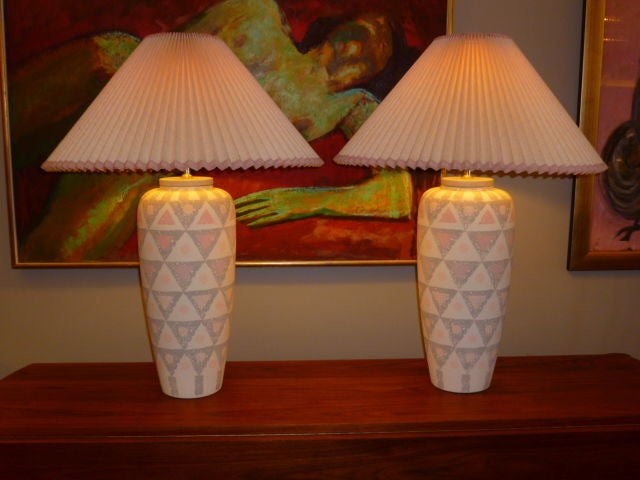 REDUCED FROM $985....Exhibiting a sleek beautiful form, this pair of vase shaped ceramic lamps have a wonderful repeating painted geometric design from top to bottom in alternating light greys, off whites and coral pink, topped with a cap in grey.