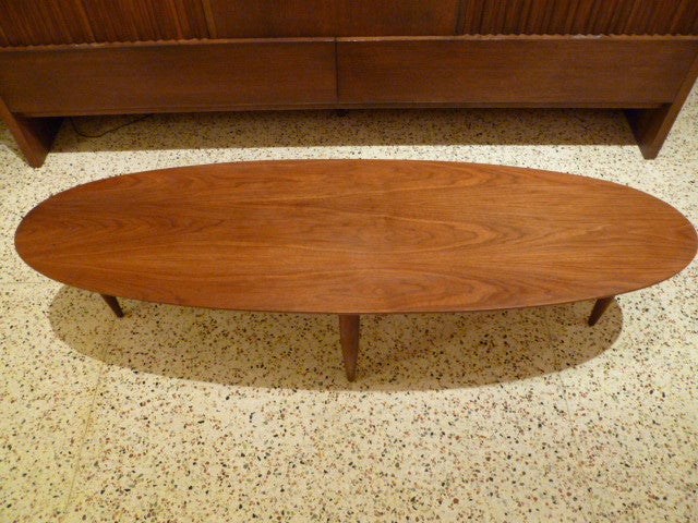SOLD JUNE 2012 Surfs up!  Beautiful and vivid figuring highlights this classic 50's surfboard shaped cocktail coffee table with deftly turned tapering solid walnut legs connected by a crossed stretcher.  Exceptional Mersman quality creation. 