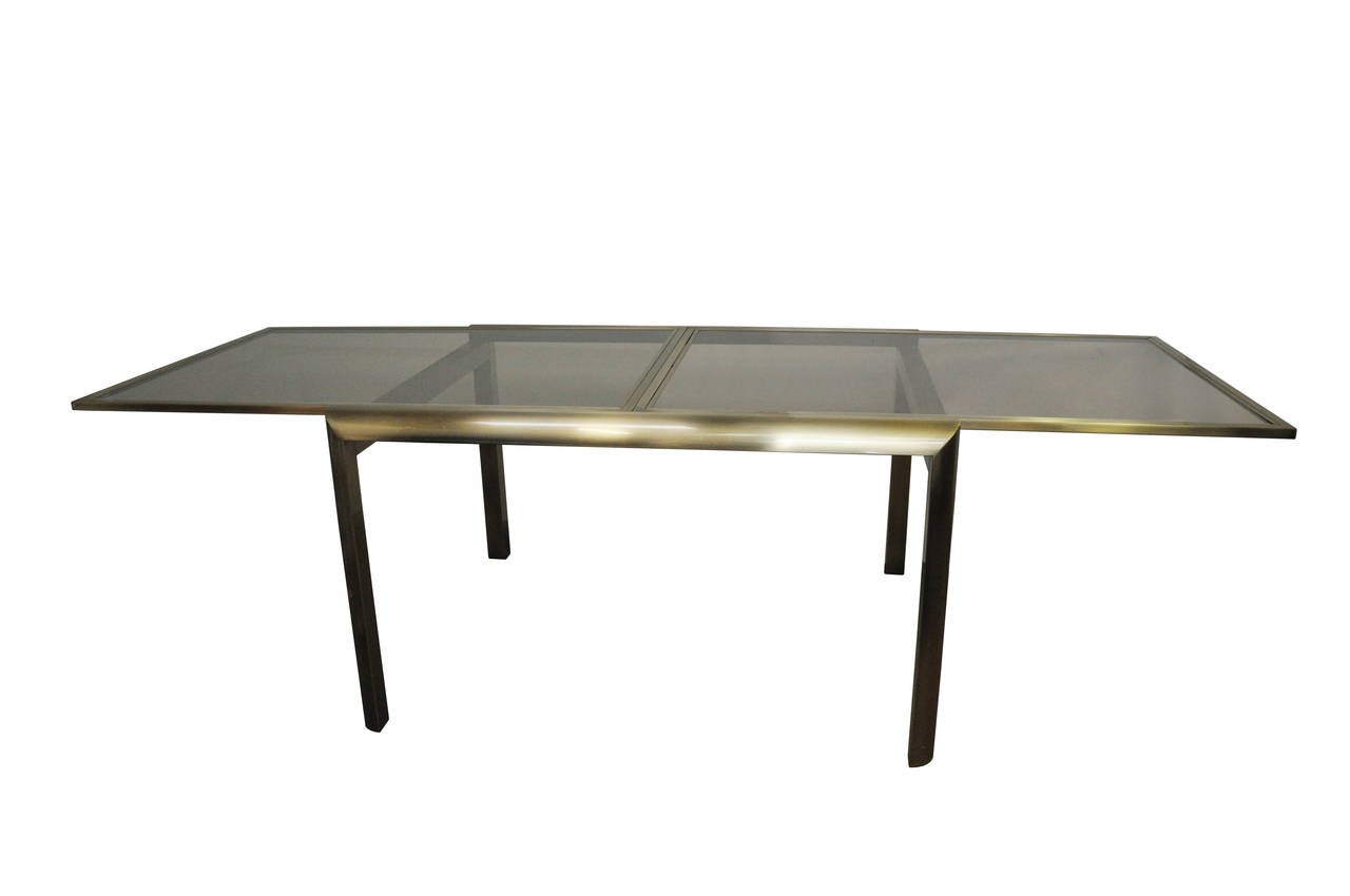 Sleek extension dining table attributed to Mastercraft. The base is brass and the glass is lightly smoked. The table extends to be 104