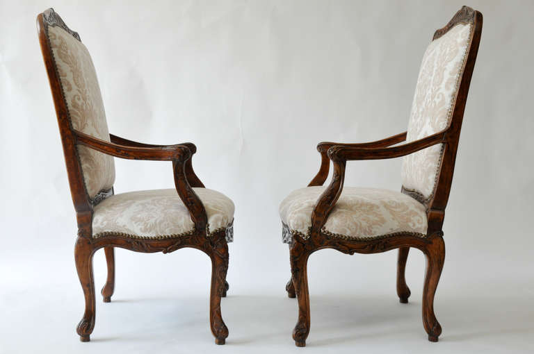 Beautiful pair of 18th century Louis XV walnut armchairs. 
Elegant hand carving to top, apron, and arms and legs. Chairs upholstered with a neutral colored ivory and taupe cotton damask. Brass nailhead trim.