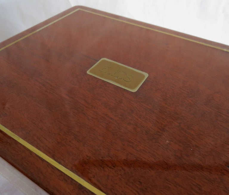 This vintage art deco Benson & Hedges cigar humidor date from ca 1925. The outer surface is mahogany with brass banding, The brass lock and key are present. The interior is tin lined and has a green felt grove where the top closes, assuring a tight