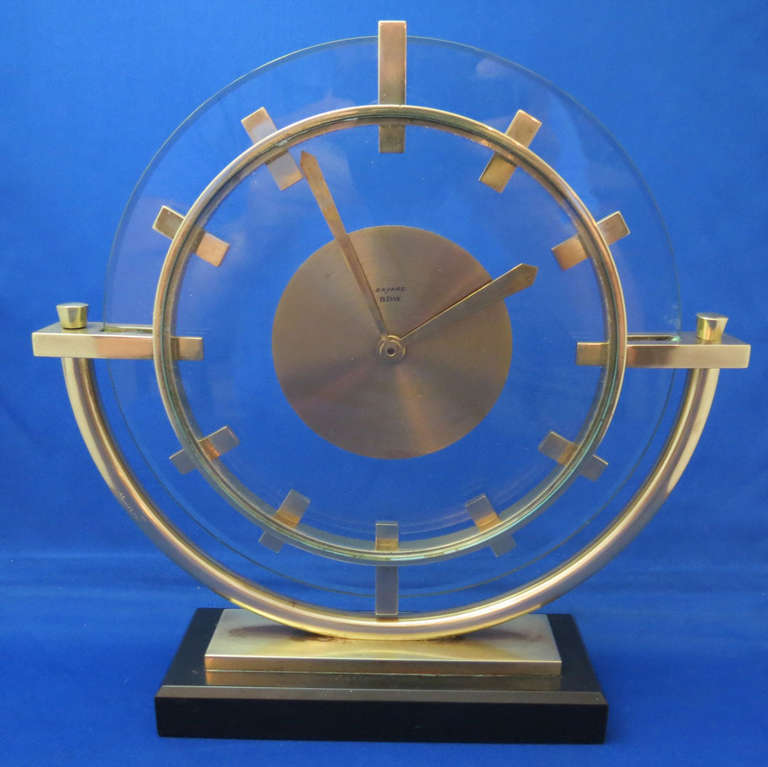 A fine French Art Deco eight day clock from the 1930’s by Bayard. The clock sits on a black marble base and a semi-circle of brass tubing holds the works and a glass and brass face with machine age brass bars representing the numbers. It keeps time