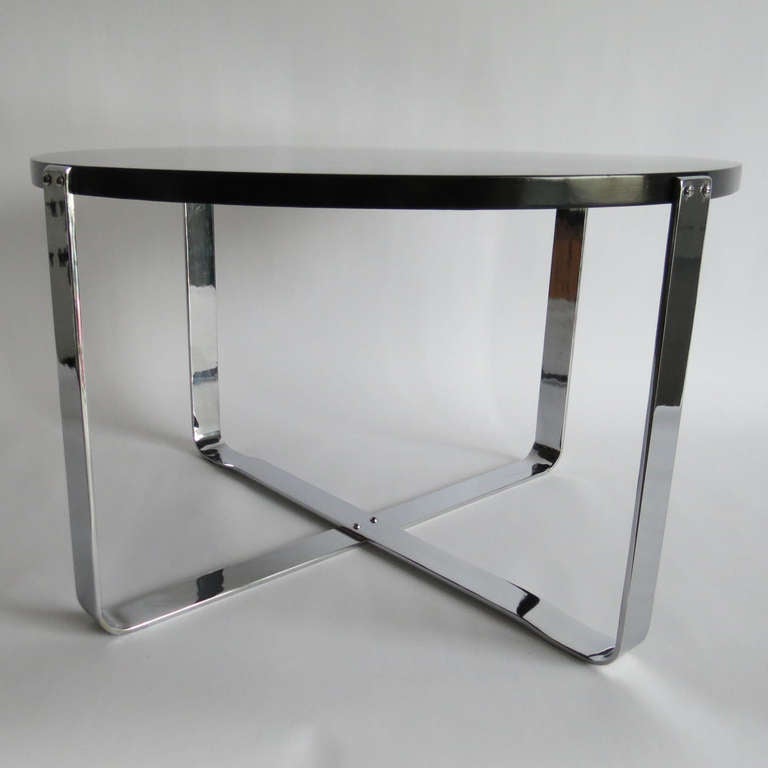 This American art deco coffee table is from the 1930’s. The circular black top is supported by flat bands of chrome steel which cross at the bottom and attach to the sides of the top. The table is 26 ¼” in diameter and 16 ¼” high. It has been