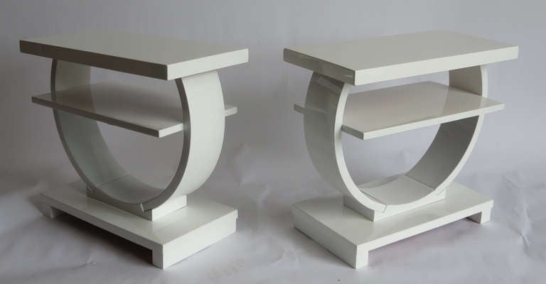 This pair of white lacquer American art deco end tables was made for and retailed by the Modernage Furniture Company in New York City, the largest “Moderne” furniture store in America in the 1930’s.  The curved supports link the rectangular base