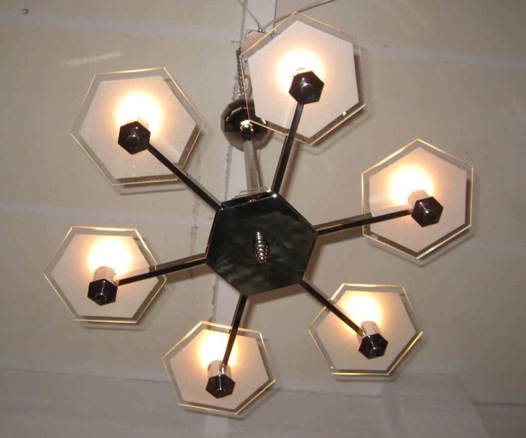 This 1930’s French art deco modernist chandelier has it in “sixes”. The bright nickel body hangs from a six sided shaft with six arms emanating from a six sided center, at the outer end of the arms are six sided sockets for the bulbs. The bulbs are