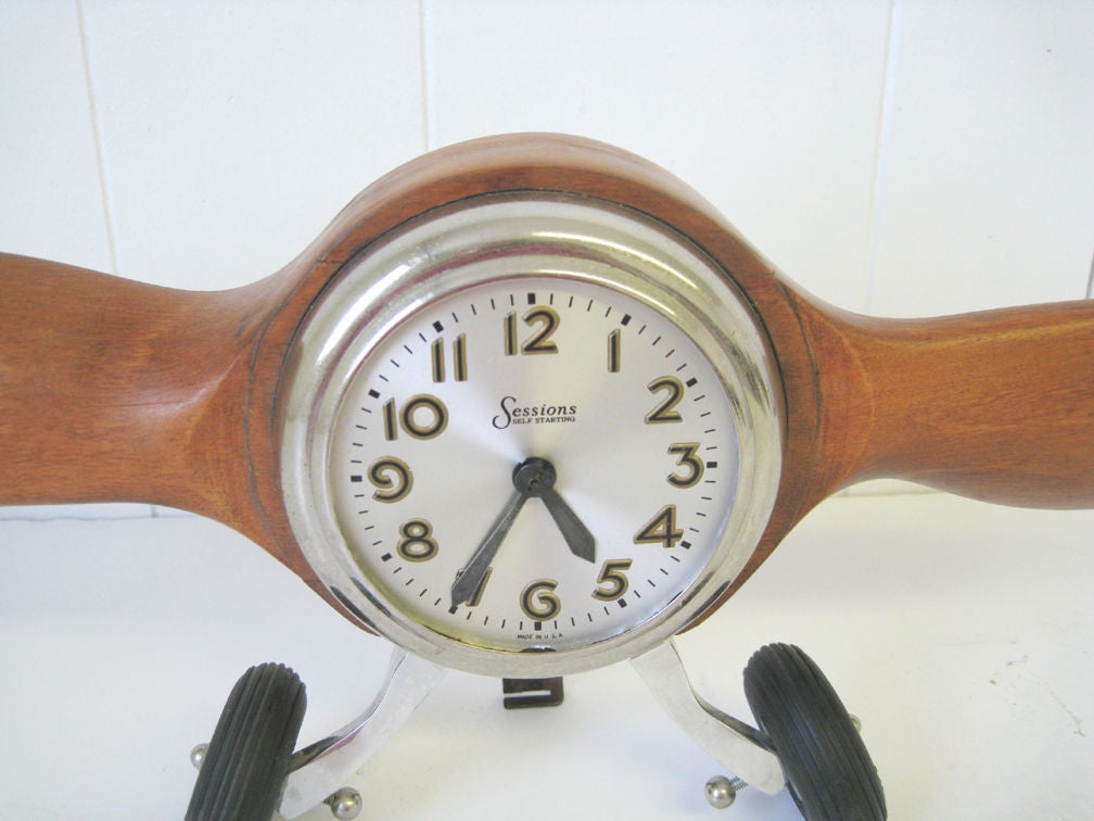 A very unusual clock. The clock face is centered on a 27” wide hard wood propeller and supported by two splayed wheels with rubber tires. The clock is marked “Sessions”, “Self Starting” and “Made in USA” and sits 8” high.