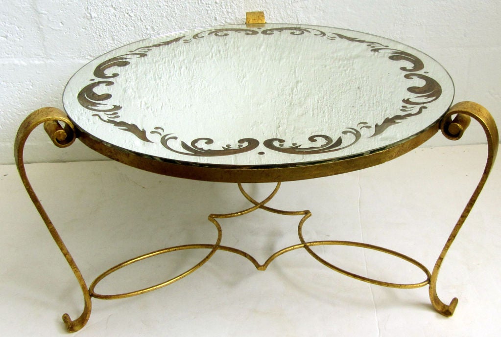 This French art deco cocktail table was designed by René Drouet (1899 – 1993) ca. 1939.   The wrought iron base is gilded in gold leaf.  The mirror top is etched from the bottom in arabesque designs filled with gold leaf.  The table is 14” high and