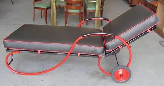 This 1930's American art deco chaise lounge is a machine age symphony in black and red. Constructed of rolled steel rods with an unusual sprung seat and back between flat steel frames.  The chaise rolls on two wheels with tires in excellent