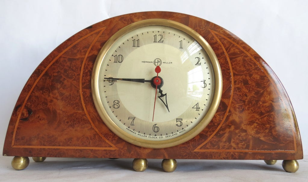 Gilbert Rohde designed this rare demilune clock for the Herman Miller Clock Company in Zeeland, Michigan.  It is pictured in their 1935 and 1937 catalogs and is shown as # 4718.  The front is maple burl with an inlaid line of Sapai wood.  The dial