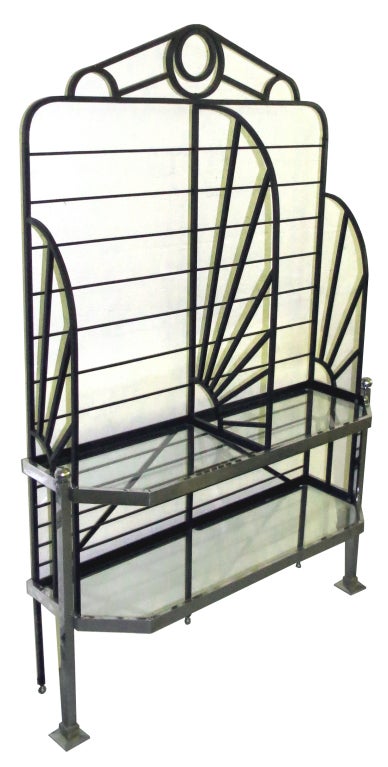 This French art deco display rack is from the 1930’s.  It is constructed of black hand wrought iron with chrome front legs and chrome borders in front of two glass shelves.  The sides and center dividers are fashioned in a sunburst design.  The rack