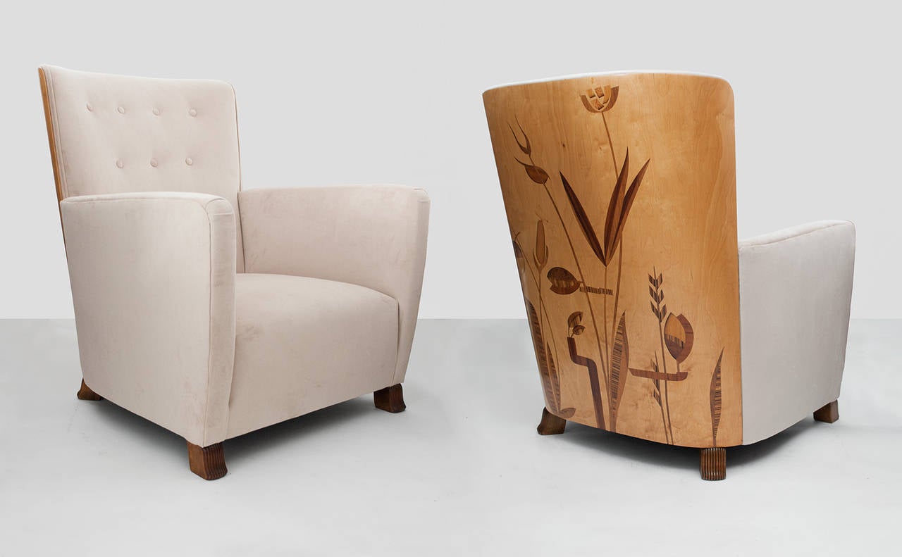Important pair of Swedish Art Deco lounge chairs with curved marquetry backs. Chairs were designed by Erik Chambert and feature a design of water plants on their curved backs. Feet are solid wood and finely carved. These chairs were produced in very
