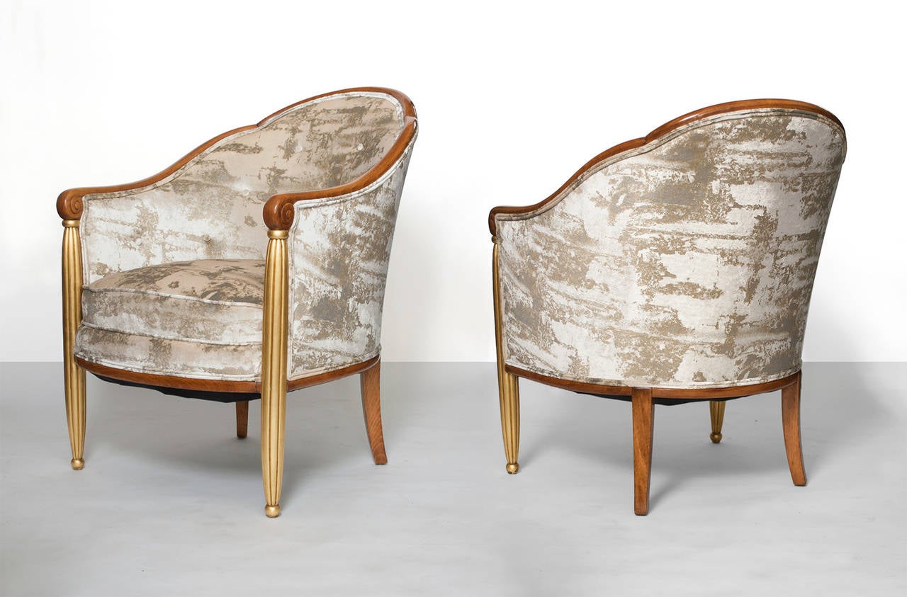 Pair of French Art Deco parcel-gilt and upholstered bergères, circa 1920s. The chairs have front reeded columns in gilt, scrolled backs and sabre rear legs are carved maple. Height: 32