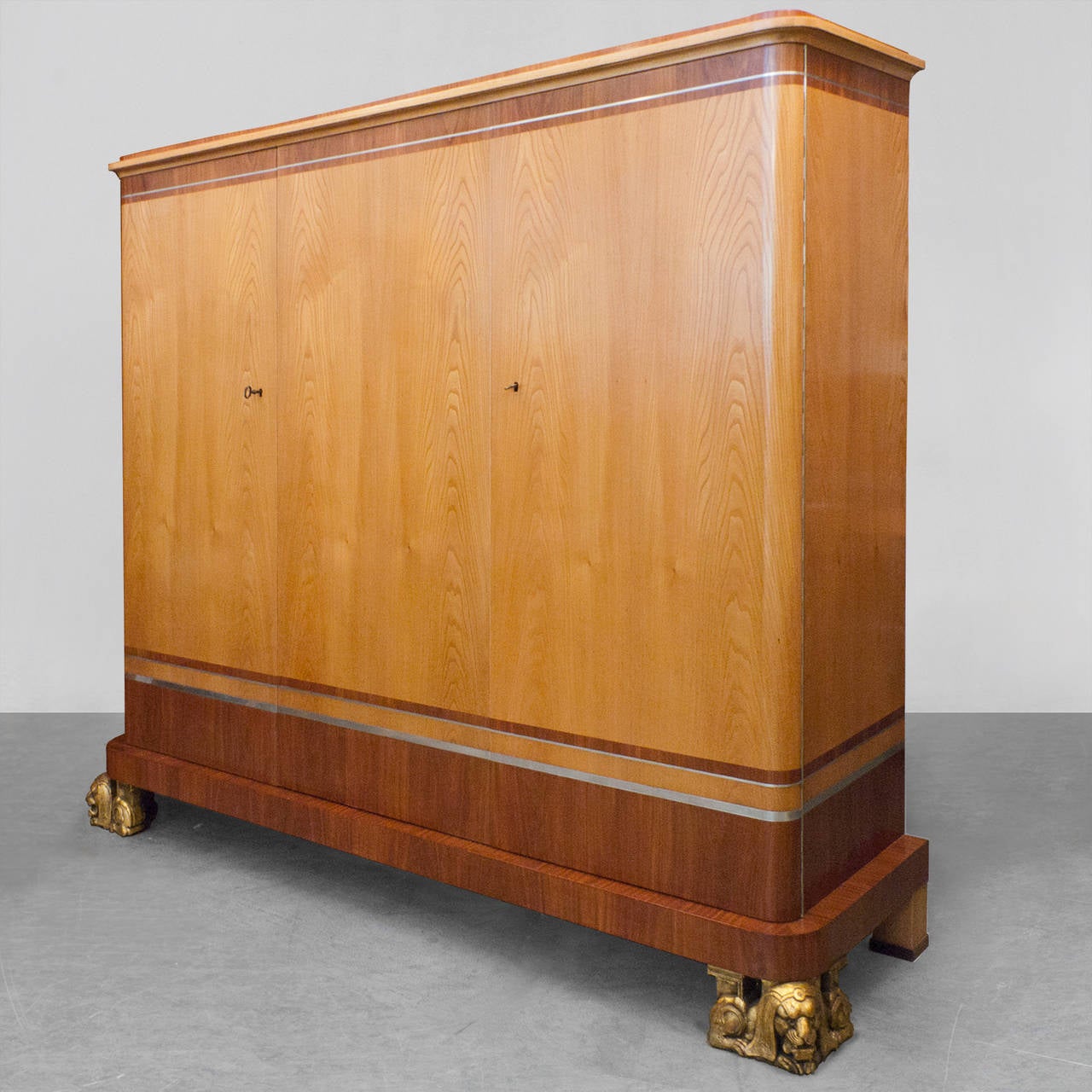 Fantastic Swedish Art Deco 3-door cabinet designed by architect Carl Bergsten. The cabinet is veneered in elm and mahogany and inlayed with bands of pewter. The two front feet are carved gilt wood in the form of resting lions. Double doors on the