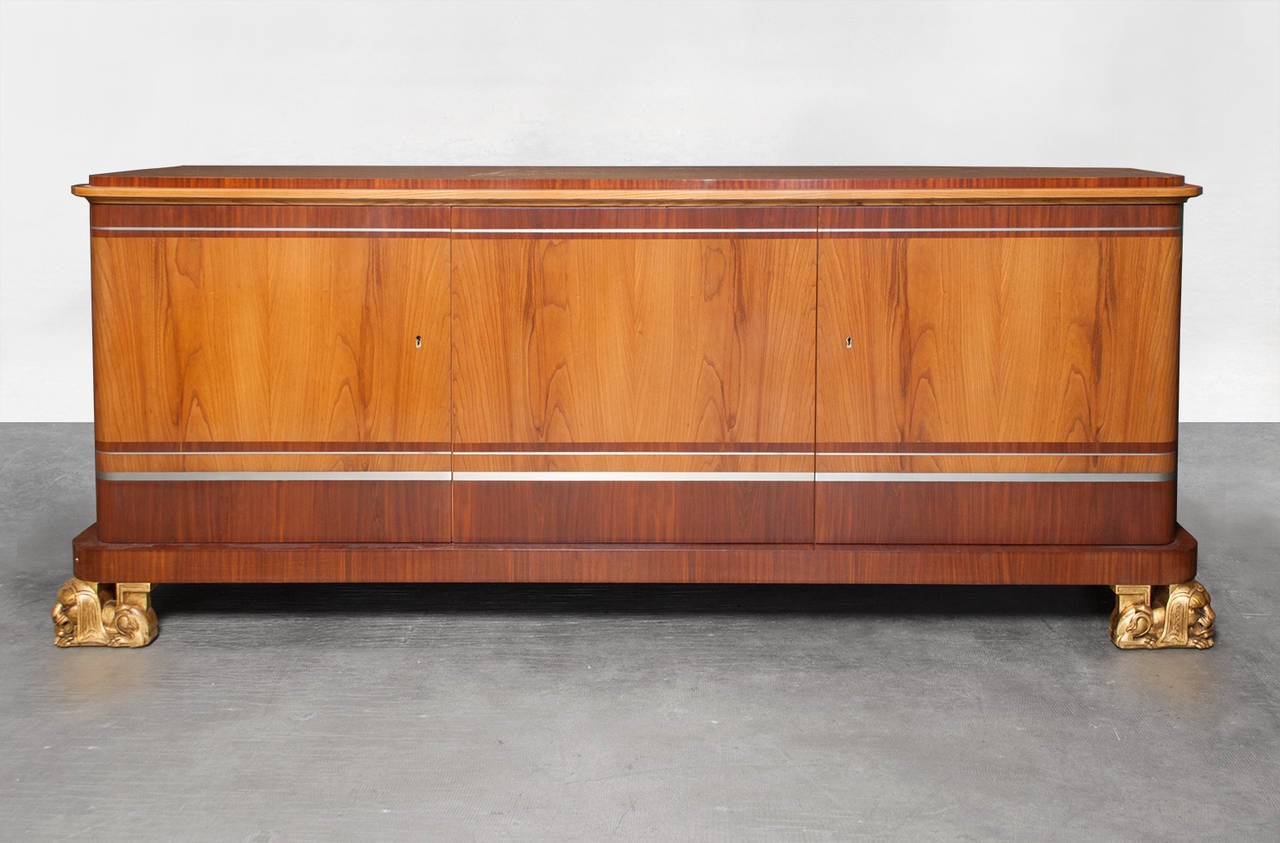 Fantastic Scandinavian Modern, Swedish Art Deco three-door sideboard cabinet designed by architect Carl Bergsten. The cabinet is veneered in elm and mahogany and inlaid with bands of pewter. The two front feet are carved giltwood in the form of