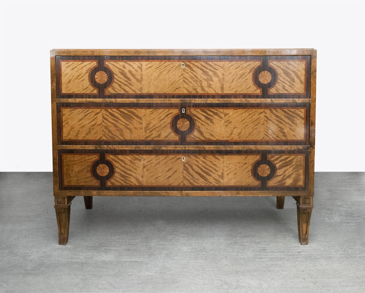 A Swedish Art Deco chest of drawers with marquetry in Macassar ebony, rosewood and other woods. The chest's design is in the manner of early Carl Malmsten's designs made by Bodafors. Made from solid stained birch the chest features four carved sabre