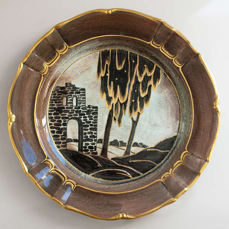 A large Scandinavian Modern, Swedish art deco ceramic charger depicting a landscape with stone ruin and 2 trees in the foreground. Hand decorated and detailed in gold on a green and brown luster glaze ground, dated 1937.
 
Diameter: 12",