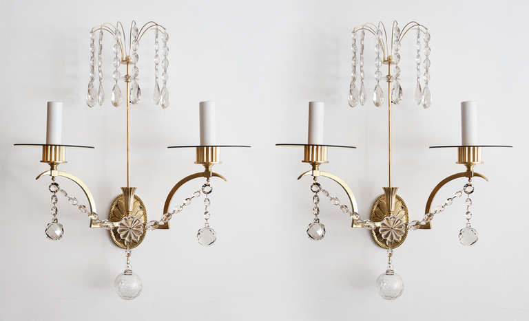 Large pair of finely detailed Swedish art deco double arm wall sconces. Each sconce has a pair of arched arms which hold a gold glass bobeches and Edison base sockets covered in white candle sleeves. Swags of crystals connect the arms and each arm