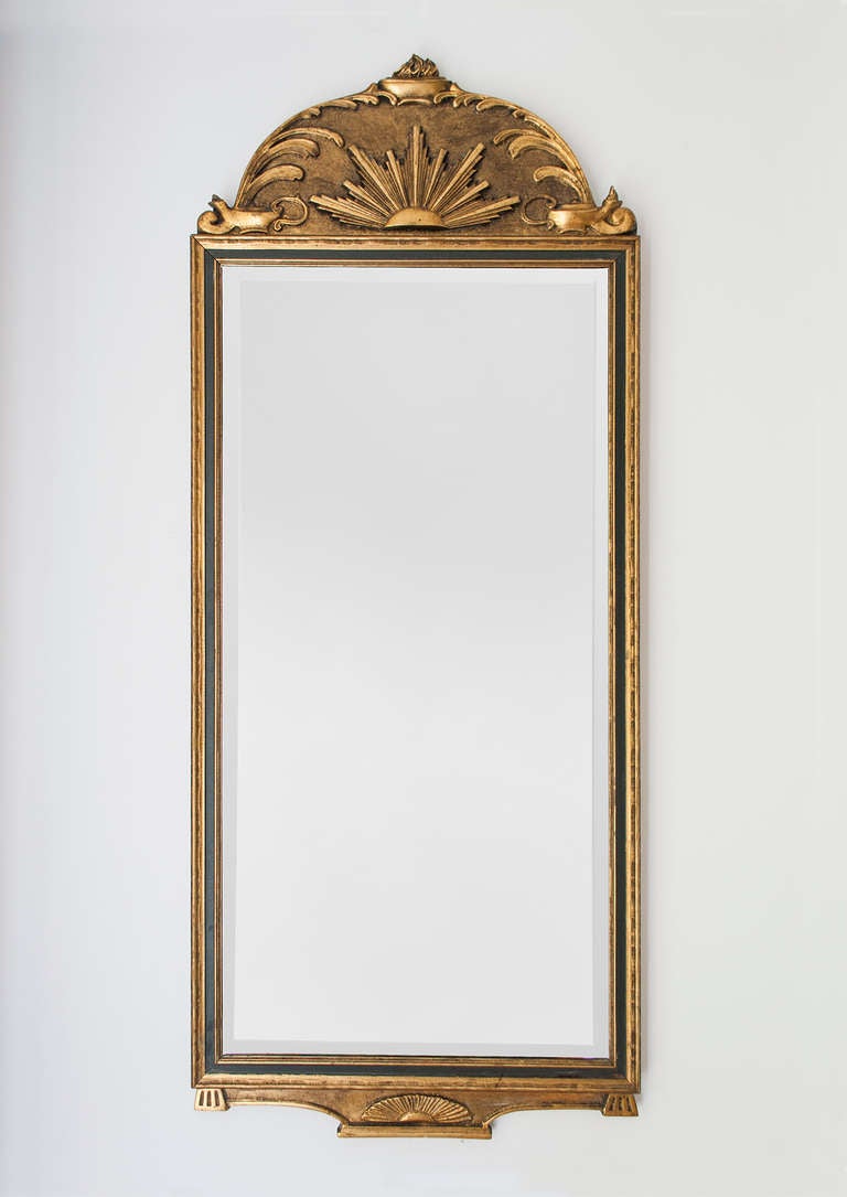 Delicate gilt wood Swedish Art Deco wall mirror with cared details depicting a sunburst and ancient oil lamps. Mirror glass is original and has a one inch beveled edge. Height: 39, Width: 16