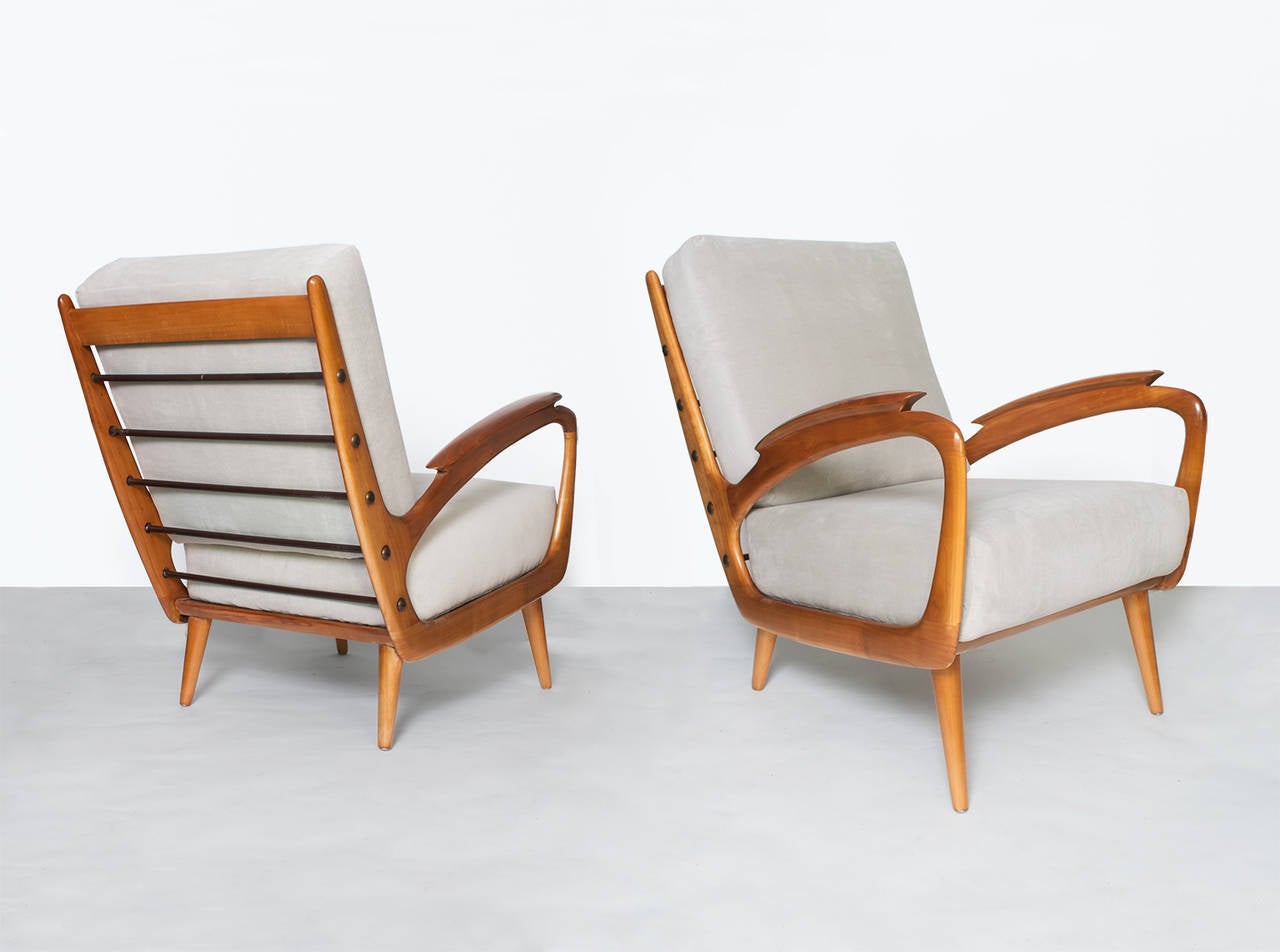 Sleek and dynamic pair of carved wood Mid-Century Modern armchairs from France. The chairs design plays with negative space and are reminiscent of the works of sculptor Henry Moore. A series of vinyl wrapped coil springs with patinated brass disc