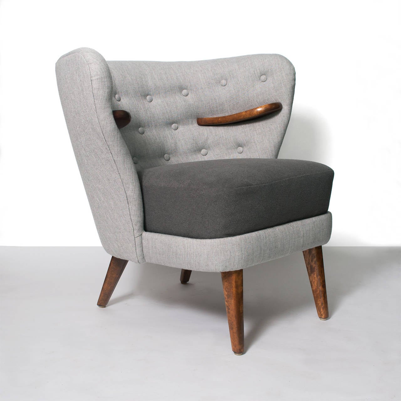 A Scandinavian modern mid-century wrap around wing chair with carved internal arms. This chair is detailed with 3 rows of button and a contrasting wool upholstered seat cushion. Arms and legs are stained solid birch. Newly upholstered and restored,