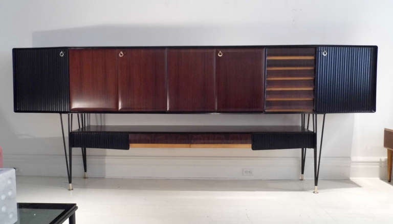 Large sideboard or credenza. Rosewood and black ebonized, corrugated panels. Six shelving units with original brass keys plus six drawers. Four drawers at the bottom panel.
Black metal legs with brass adjustable feet. Birch wood interiors.