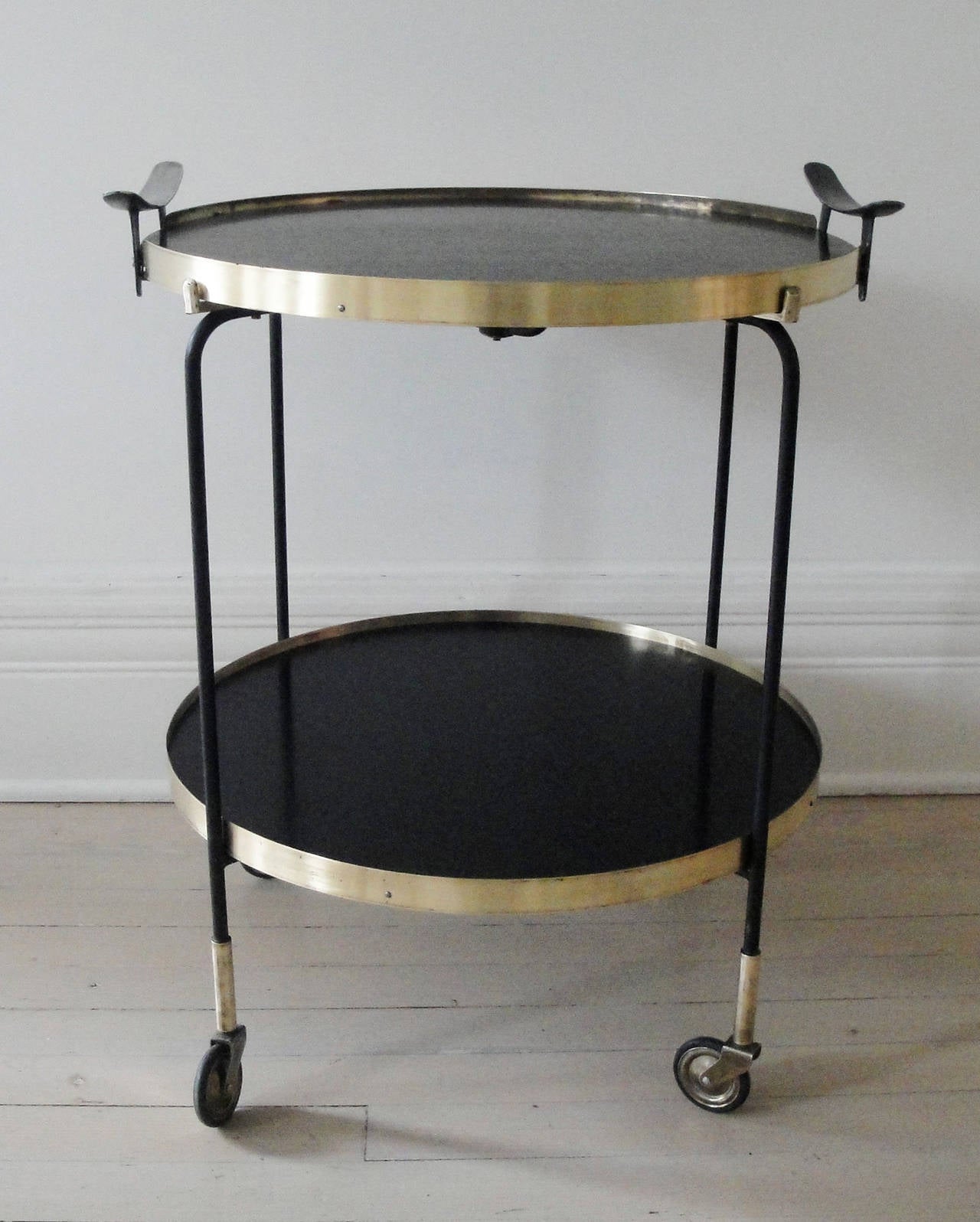 Round double-tier Italian bar cart from 1960s. Brass and black lacquered metal structure. Wooden trays with brass fittings. Removable top tray with metal handles.