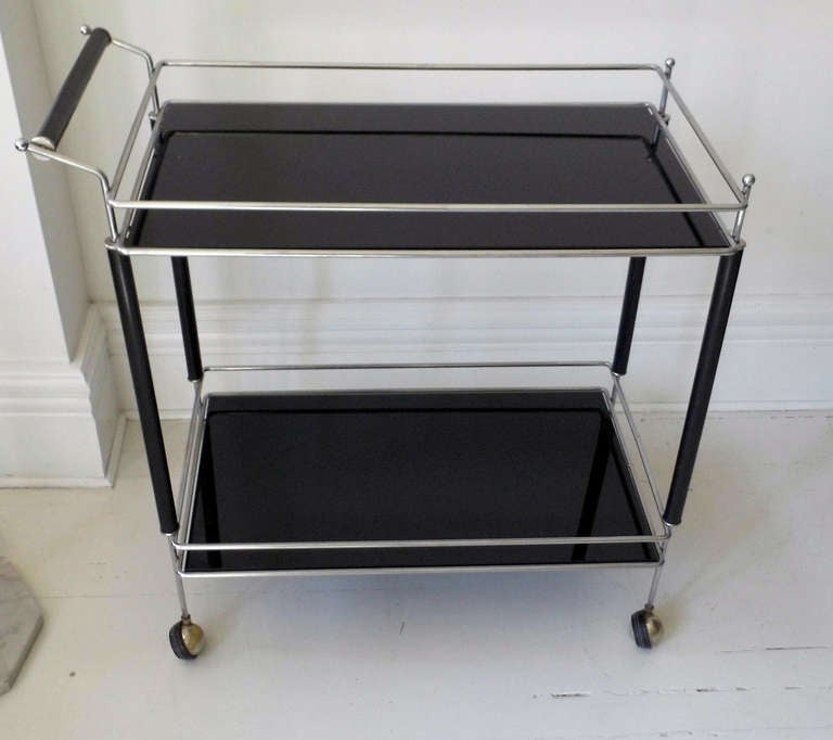 Chrome bar cart on casters. Ebonized wood and two black glass tiers.