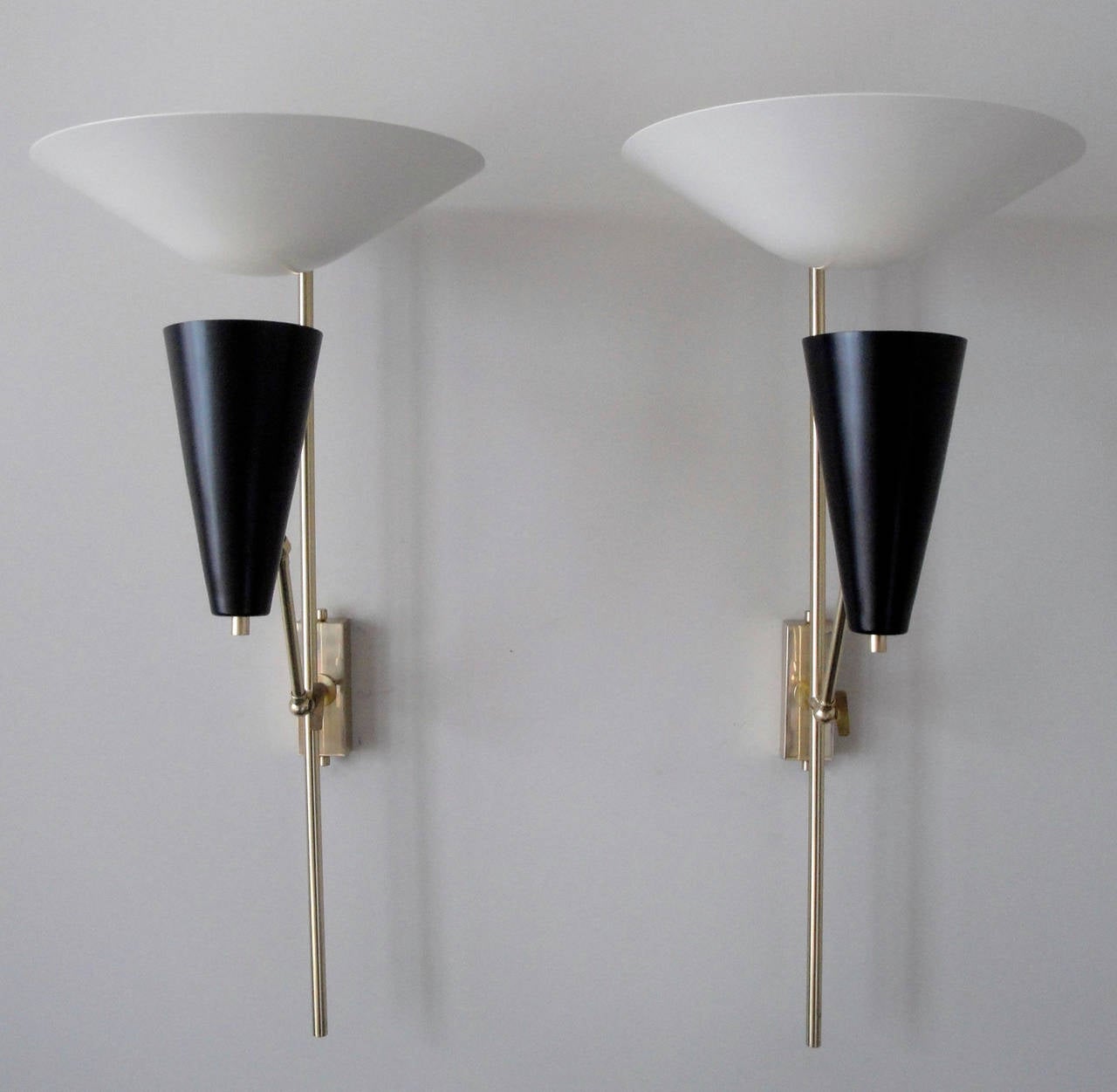 A pair of sconces with white deflector and movable black metal shades. Brass structure with pivots accommodating different positions for black shade.