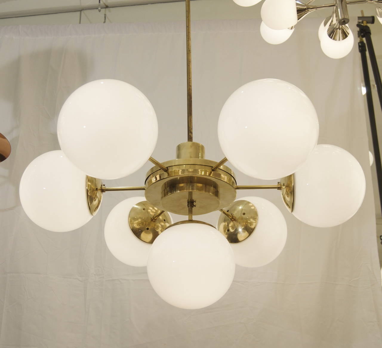 A pair of truly unique Bauhaus style Weimar era chandeliers in high polished brass, radiating six gloss white globes from the central disc body with a seventh globe downward.

Fully original solid brass construction, original globes and