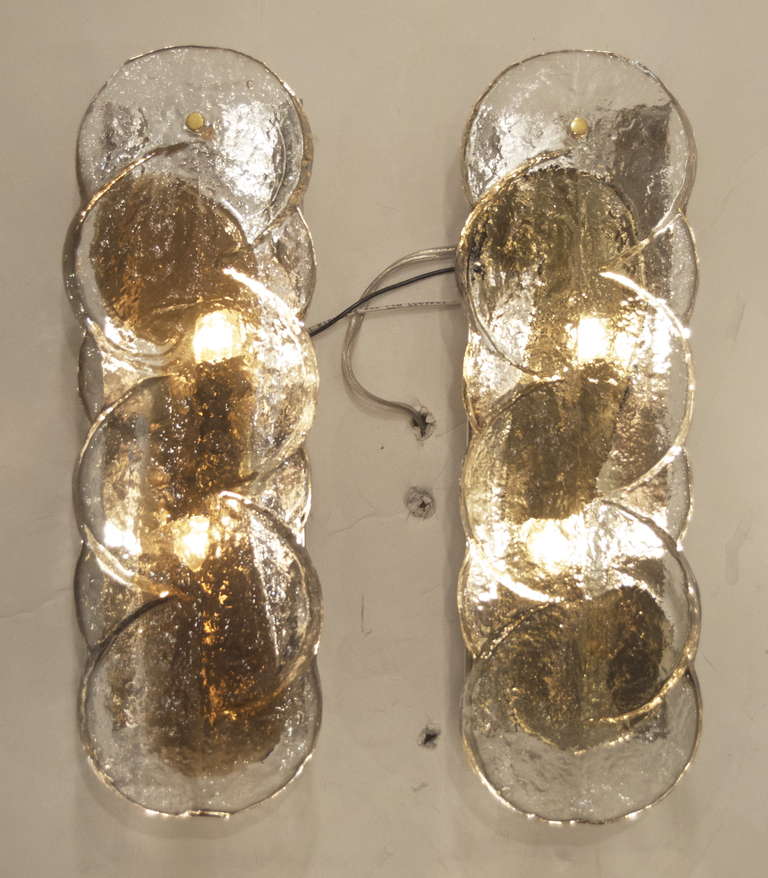 A pair of Kalmar sconces with swirl patterned glass; the heavy glass piece having a fused smoke/amber tone design similar to a violin F hole. Visible portion of backplate is gold tone.

Please note due to the hand made nature of the glass, there