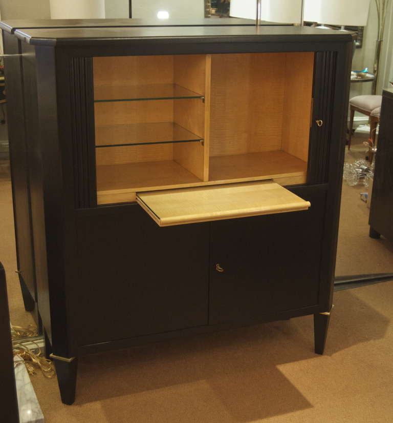 An excellent bar cabinet, ebonized exterior with brass accents, the interior in wood and glass.

Top has tambour doors which open to reveal glass shelving, a bottle area and a pull-out shelf for serving. Lower doors open for additional