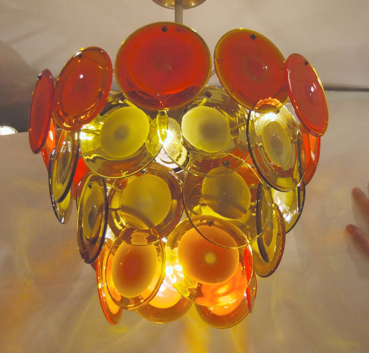 This unique Vistosi chandelier, glass being the preferred screw mounting rather than hooks features four tiers of alternating red or orange and amber or green tone, handblown glass discs on a brass fixture. The top tier of 12 discs is a strong red,