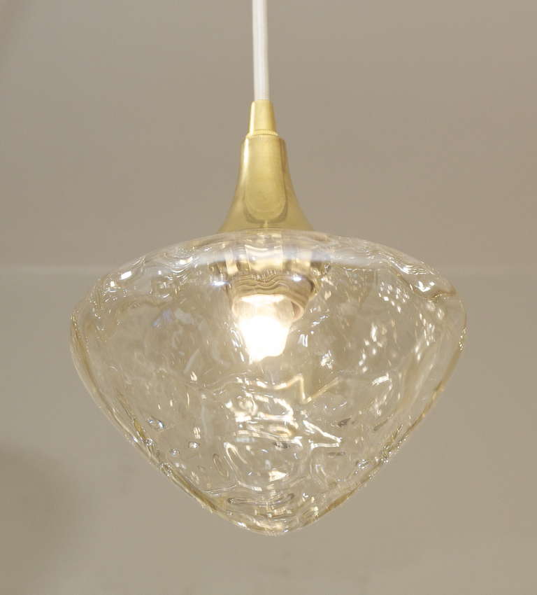 An excellent textural pendant light. Inverted teardrop form with heavy ripples in the glass surface, capped by a trumpet formed brass mount.

Perfect for kitchen islands and more.

Takes an E-14 base bulb up to 40 watts. New wiring. Currently wired