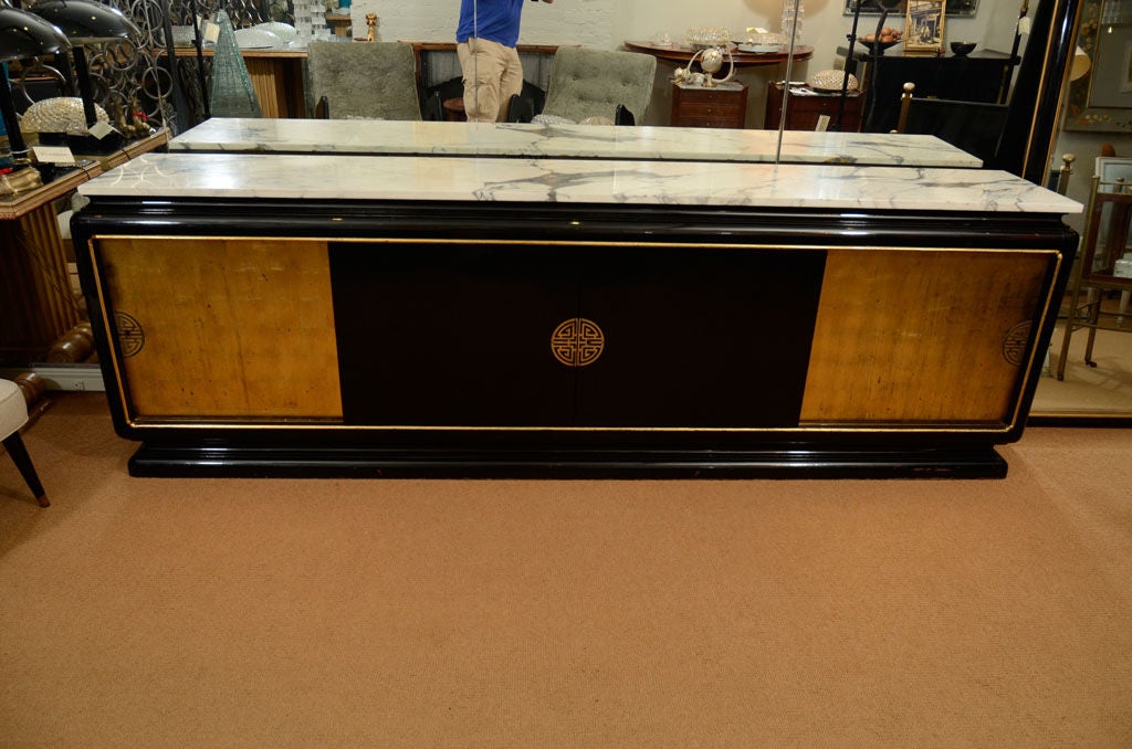 Graceful lacquer and gilt credenza with marble top.  Plentiful storage is hidden behind 4 sliding doors.  Two center doors meet with a metal Chinese-style crest.