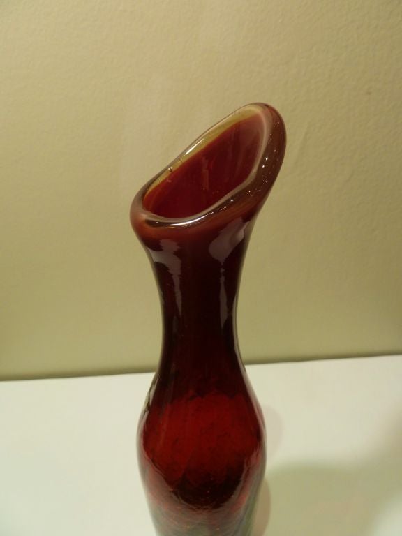 Ruby red art glass vase designed Blenko Glass.  Cylinder shape with elongated neck and a flared asymmetrical mouth.  Stunning crackle finish is seen within a slight spiral pattern inside the piece.  Vase features the original 'Blenko Handcraft' foil