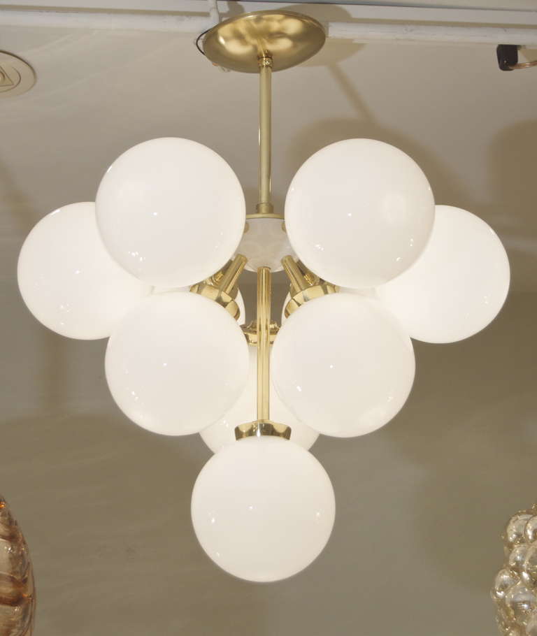 An elegant chandelier in the form of an inverted pyramid, 10 gloss opal globes capping brass arms extending from a hemispherical white enameled body.

Takes 10 E-14 base bulbs up to 40 watts per bulb, new wiring.

Height is of chandelier body