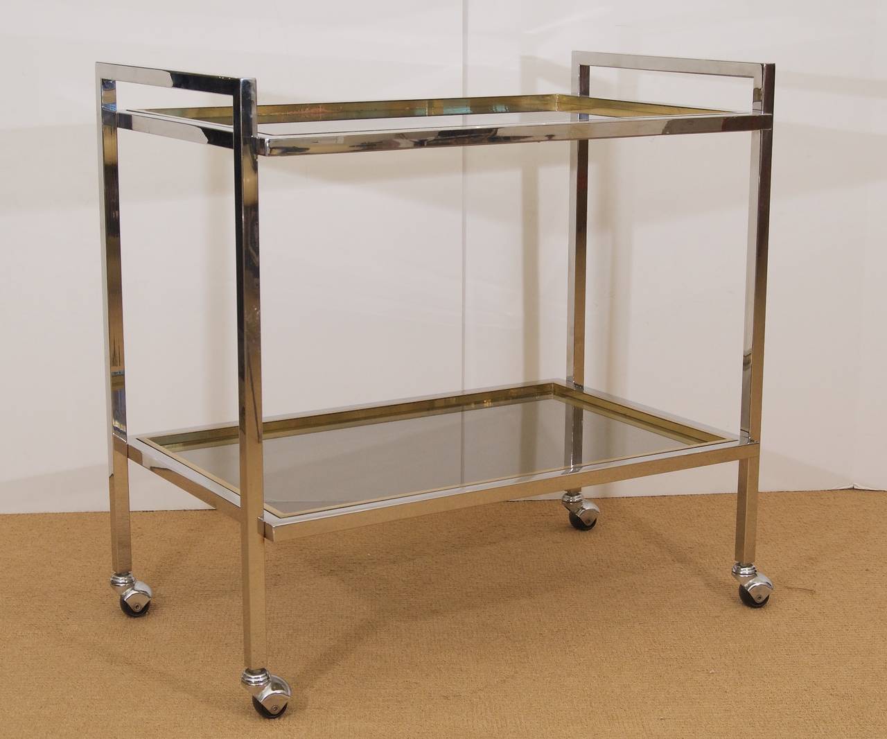 Two-tiered brass and chrome bar cart with inset smoked glass tiers, attributed to Romeo Rega. The clean lines and exquisite proportions of this piece add elegance to any space.