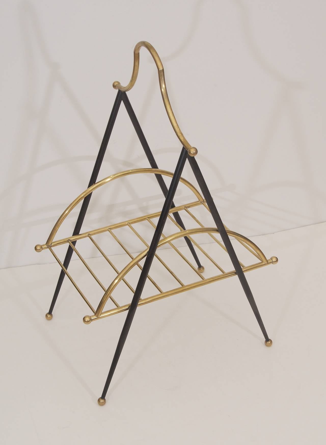 An elegant and eclectic magazine rack made with brass and black metal boosts linear and arced lines. This fantastic piece could also be put to use as a towel rack in a bathroom as an alternative.