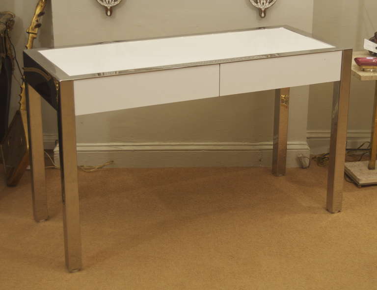 A well formed desk, formed primarily of chromed welded steel, with white laminate inserts on top and drawer fronts. Two drawers on seat side; obverse is finished and fully chrome.